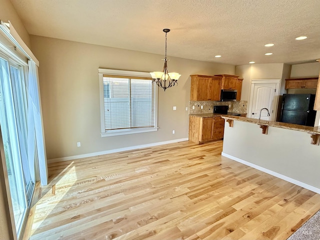 1241 W Ann Taylor St, Meridian, ID 83646 - kitchen with freestanding refrigerator, brown cabinetry, a breakfast bar area, stainless steel microwave, and a chandelier
