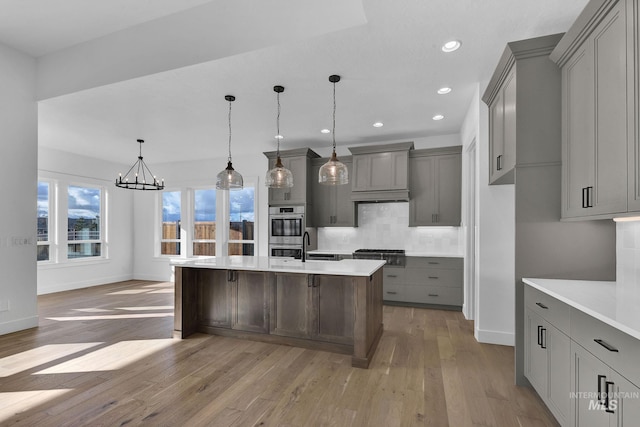 kitchen with gray cabinets, a kitchen island with sink, light hardwood / wood-style floors, and decorative light fixtures