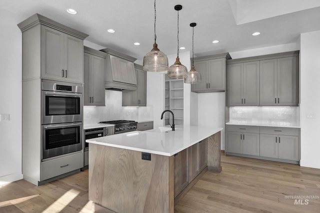 kitchen with backsplash, a kitchen island with sink, appliances with stainless steel finishes, and light hardwood / wood-style flooring