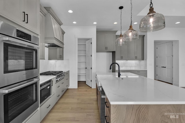 kitchen with decorative light fixtures, a kitchen island with sink, appliances with stainless steel finishes, and light hardwood / wood-style flooring