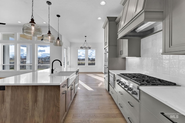 kitchen featuring light wood-type flooring, a center island with sink, stainless steel gas cooktop, and a healthy amount of sunlight