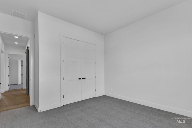 unfurnished bedroom featuring a barn door, a closet, and dark colored carpet