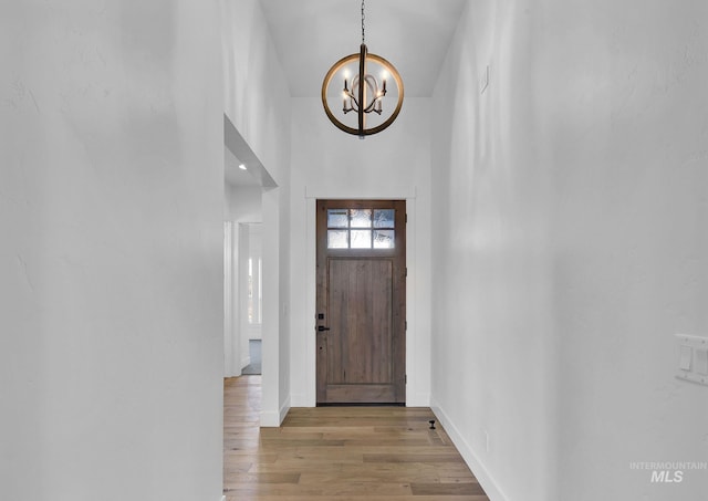 entryway with a notable chandelier, wood-type flooring, and a high ceiling