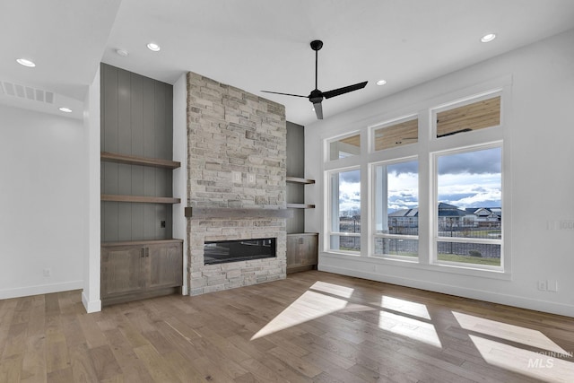 unfurnished living room with ceiling fan, light hardwood / wood-style floors, and a stone fireplace