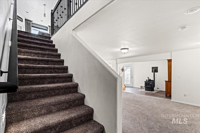 staircase featuring a wood stove, a textured ceiling, baseboards, and carpet flooring