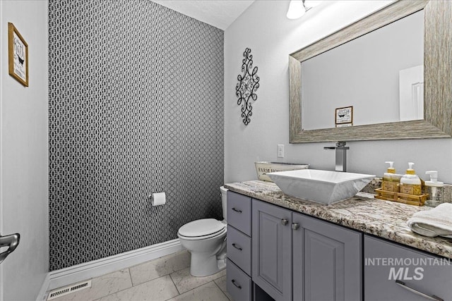 bathroom featuring toilet, vanity, visible vents, and baseboards