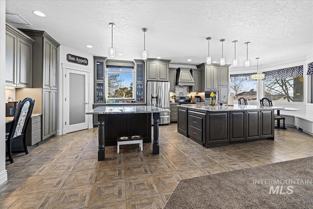 kitchen featuring light stone counters, custom exhaust hood, stainless steel appliances, an island with sink, and a kitchen breakfast bar