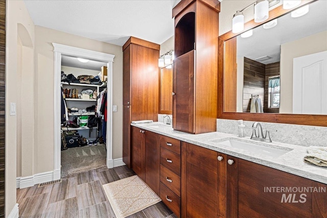 bathroom with double vanity, a spacious closet, baseboards, and a sink