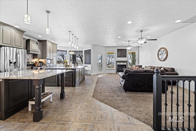 kitchen with a glass covered fireplace, an island with sink, appliances with stainless steel finishes, decorative light fixtures, and gray cabinetry