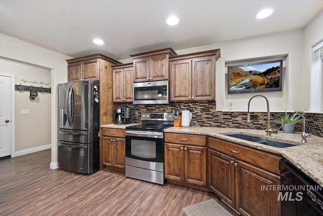 kitchen with light stone counters, dark wood-style flooring, a sink, stainless steel appliances, and tasteful backsplash