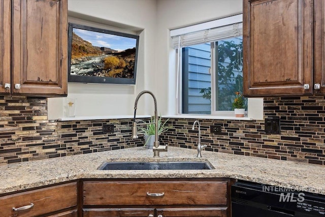 kitchen with light stone counters, black dishwasher, tasteful backsplash, and a sink