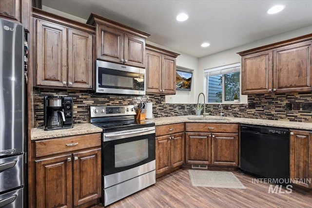 kitchen with backsplash, appliances with stainless steel finishes, wood finished floors, and a sink