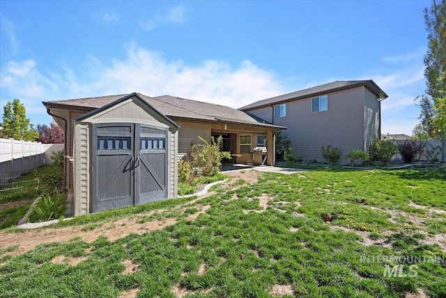 rear view of house with fence, a yard, a storage shed, an outdoor structure, and a patio area