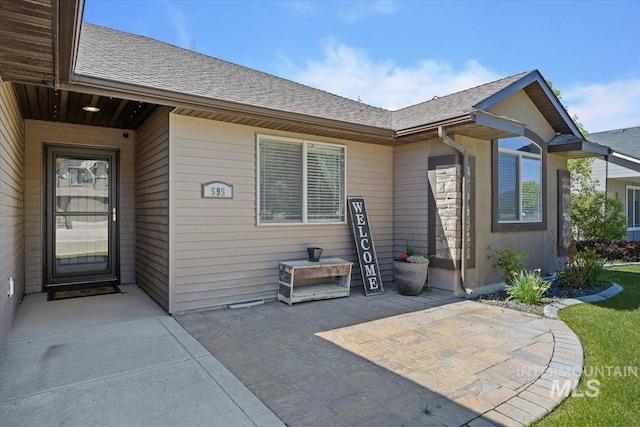 doorway to property featuring a patio and a shingled roof