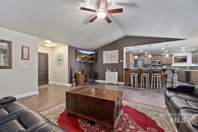 living room featuring wood finished floors, visible vents, baseboards, lofted ceiling, and ceiling fan