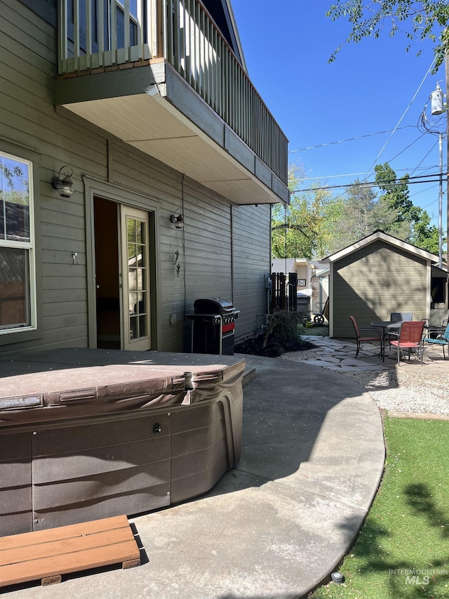 view of patio / terrace featuring a hot tub, a balcony, grilling area, and an outdoor structure