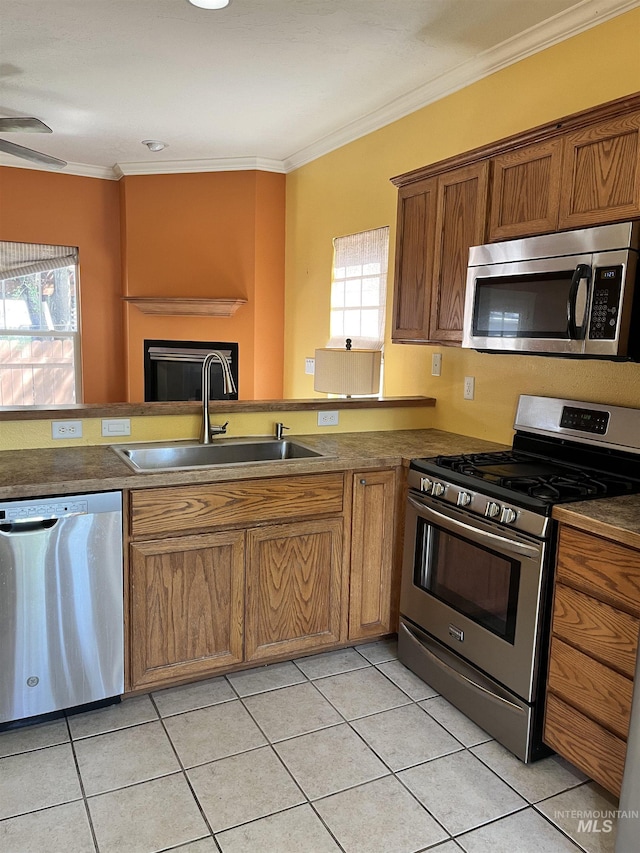 kitchen featuring appliances with stainless steel finishes, a sink, light tile patterned floors, brown cabinets, and crown molding