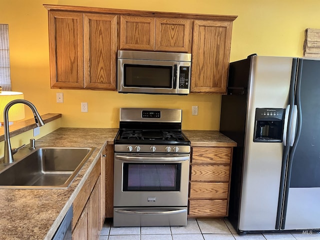 kitchen with stainless steel appliances, a sink, brown cabinetry, and light tile patterned floors