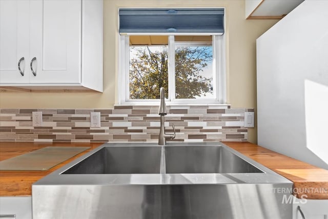 room details featuring sink, white cabinets, and wood counters