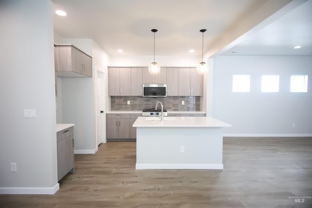 kitchen with hanging light fixtures, backsplash, an island with sink, appliances with stainless steel finishes, and hardwood / wood-style flooring