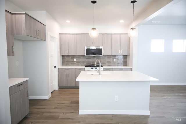 kitchen with light brown cabinetry, an island with sink, stainless steel appliances, and hardwood / wood-style flooring