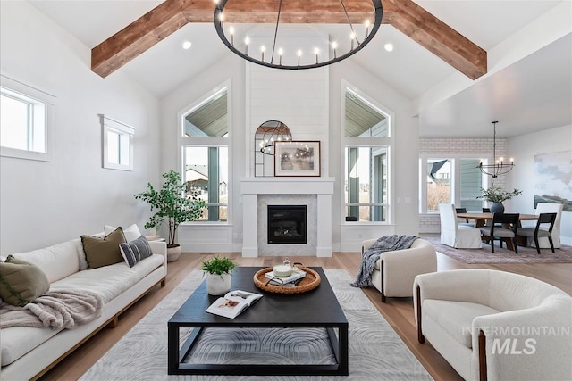 living room with a chandelier, high vaulted ceiling, a large fireplace, wood finished floors, and beam ceiling