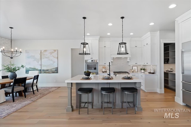 kitchen with tasteful backsplash, a kitchen breakfast bar, light countertops, light wood-style floors, and white cabinetry