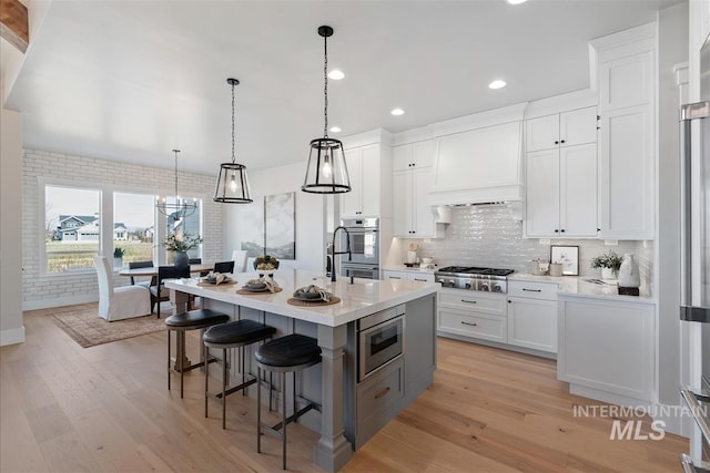 kitchen with light wood finished floors, custom range hood, stainless steel appliances, a kitchen bar, and backsplash