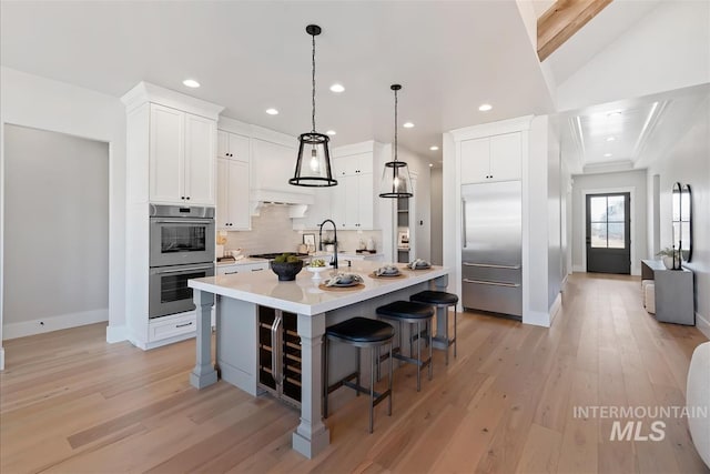 kitchen featuring stainless steel appliances, light countertops, backsplash, white cabinets, and light wood-type flooring