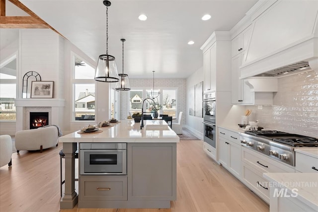 kitchen with stainless steel gas cooktop, a large fireplace, premium range hood, a sink, and light wood-type flooring