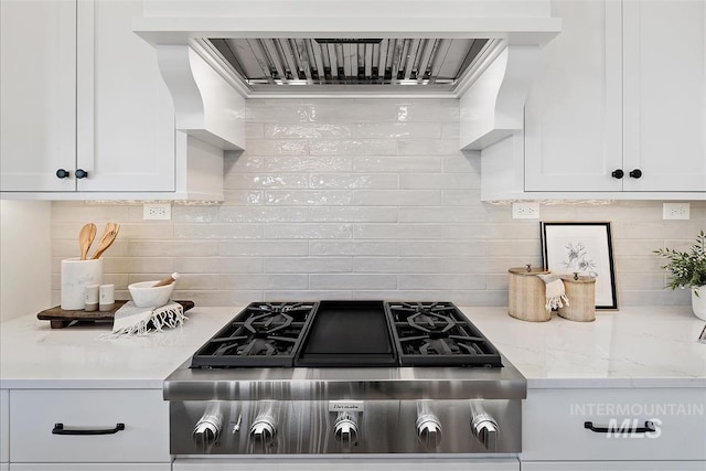 kitchen featuring light stone counters, stainless steel gas stovetop, backsplash, white cabinets, and extractor fan