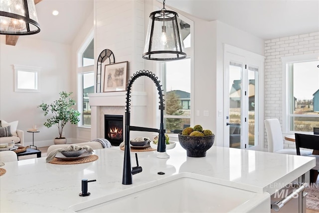 interior space featuring recessed lighting, a sink, hanging light fixtures, light stone countertops, and a glass covered fireplace