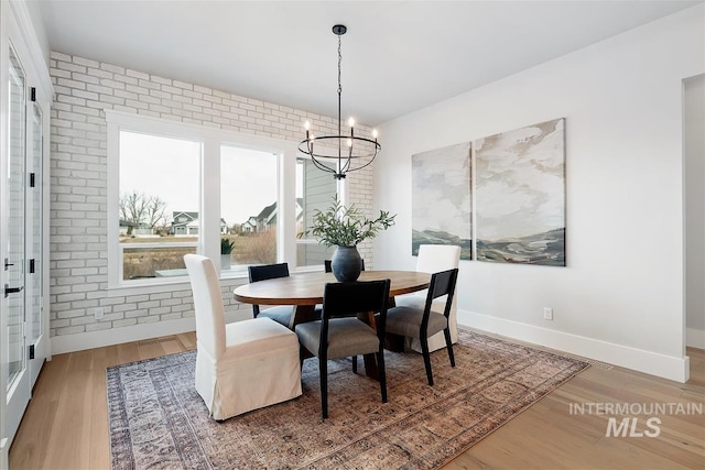 dining room featuring brick wall, an inviting chandelier, wood finished floors, and baseboards