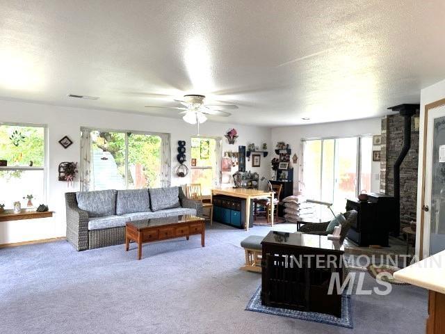 living room with carpet flooring, a wealth of natural light, a textured ceiling, and a wood stove