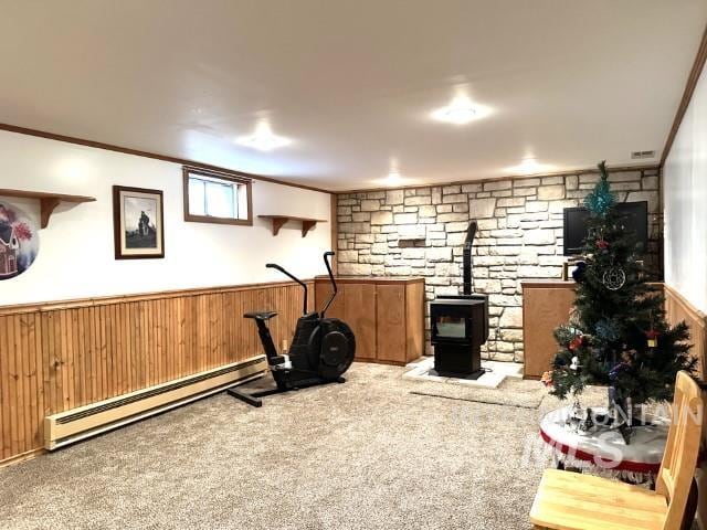 workout area featuring a baseboard radiator, carpet, ornamental molding, and a wood stove