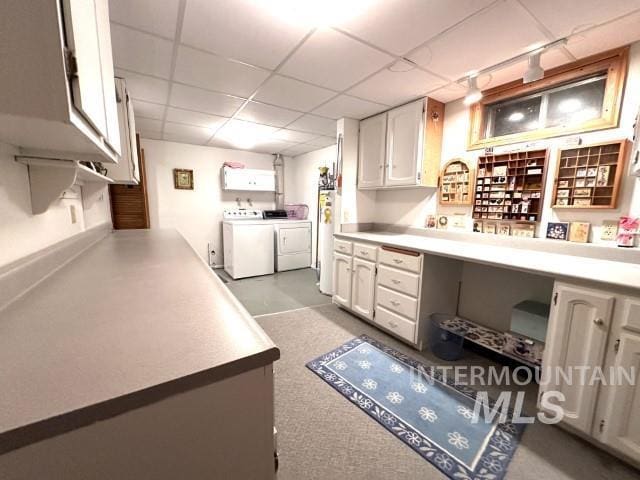 kitchen featuring gas water heater, built in desk, white cabinets, independent washer and dryer, and a drop ceiling