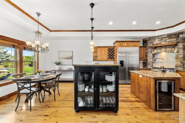 kitchen with wine cooler, pendant lighting, built in fridge, and a center island with sink