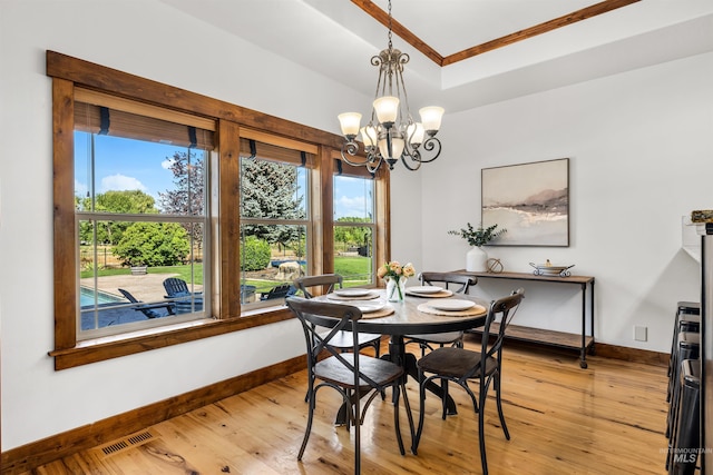 dining area with crown molding, a tray ceiling, light hardwood / wood-style flooring, and a notable chandelier