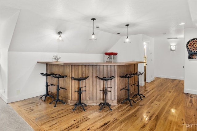 bar featuring lofted ceiling, decorative light fixtures, and light hardwood / wood-style flooring