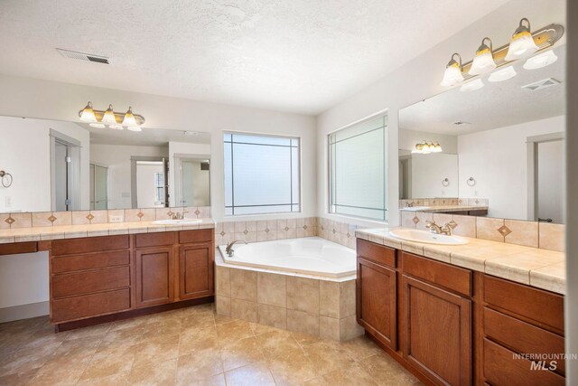 full bath with a garden tub, two vanities, tile patterned floors, and a textured ceiling