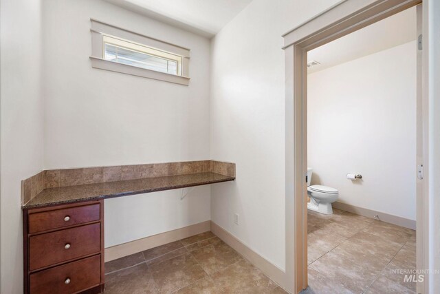 bathroom with toilet, baseboards, and tile patterned flooring