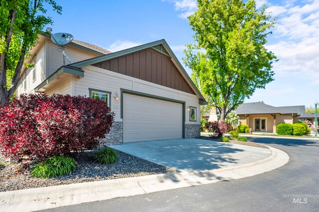 view of front facade featuring concrete driveway, an attached garage, stone siding, and board and batten siding