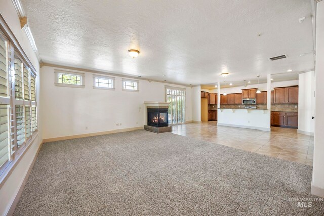 unfurnished living room featuring light colored carpet, baseboards, a multi sided fireplace, light tile patterned floors, and a textured ceiling