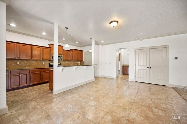kitchen featuring stainless steel microwave, arched walkways, decorative backsplash, a kitchen breakfast bar, and brown cabinetry