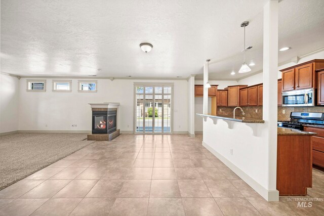 kitchen featuring appliances with stainless steel finishes, brown cabinetry, open floor plan, decorative backsplash, and a textured ceiling