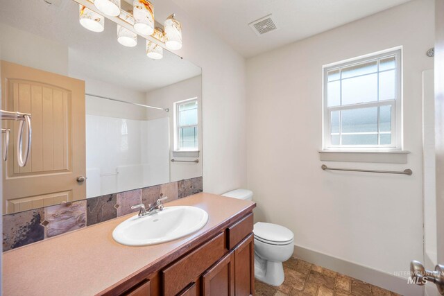 full bathroom featuring toilet, vanity, a shower, and baseboards