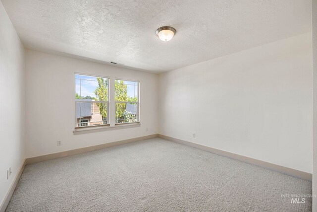 empty room with light colored carpet, a textured ceiling, and baseboards
