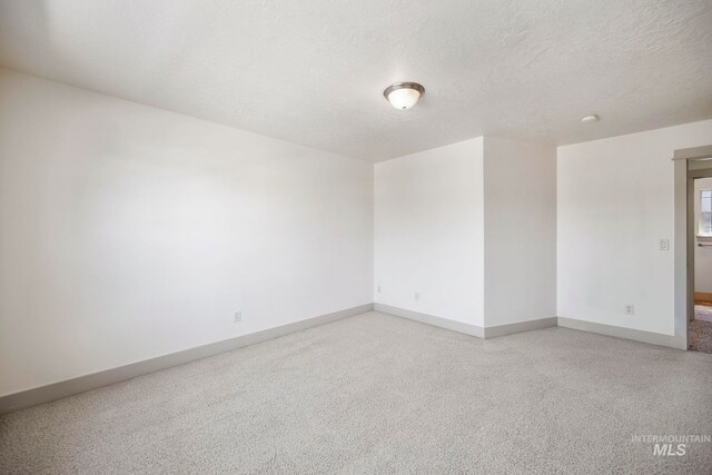 unfurnished room with baseboards, a textured ceiling, light carpet, and a smoke detector