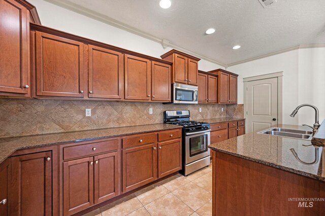 kitchen with stainless steel appliances, a sink, ornamental molding, brown cabinetry, and tasteful backsplash