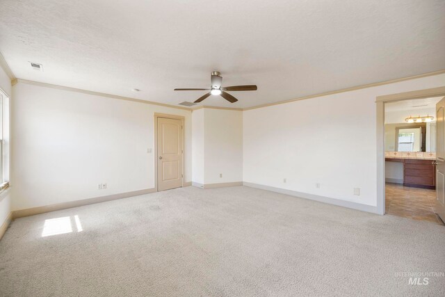 empty room featuring crown molding, light carpet, a ceiling fan, and baseboards